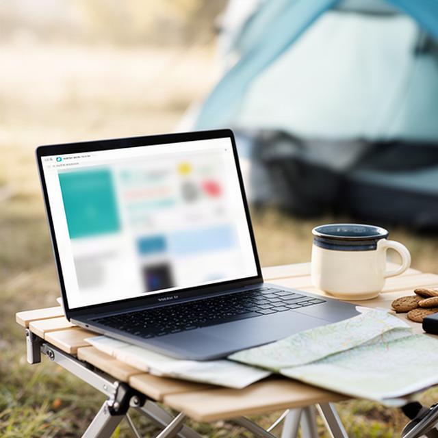 Laptop mit geöffneter Website neben einer Tasse auf einem Campingtisch